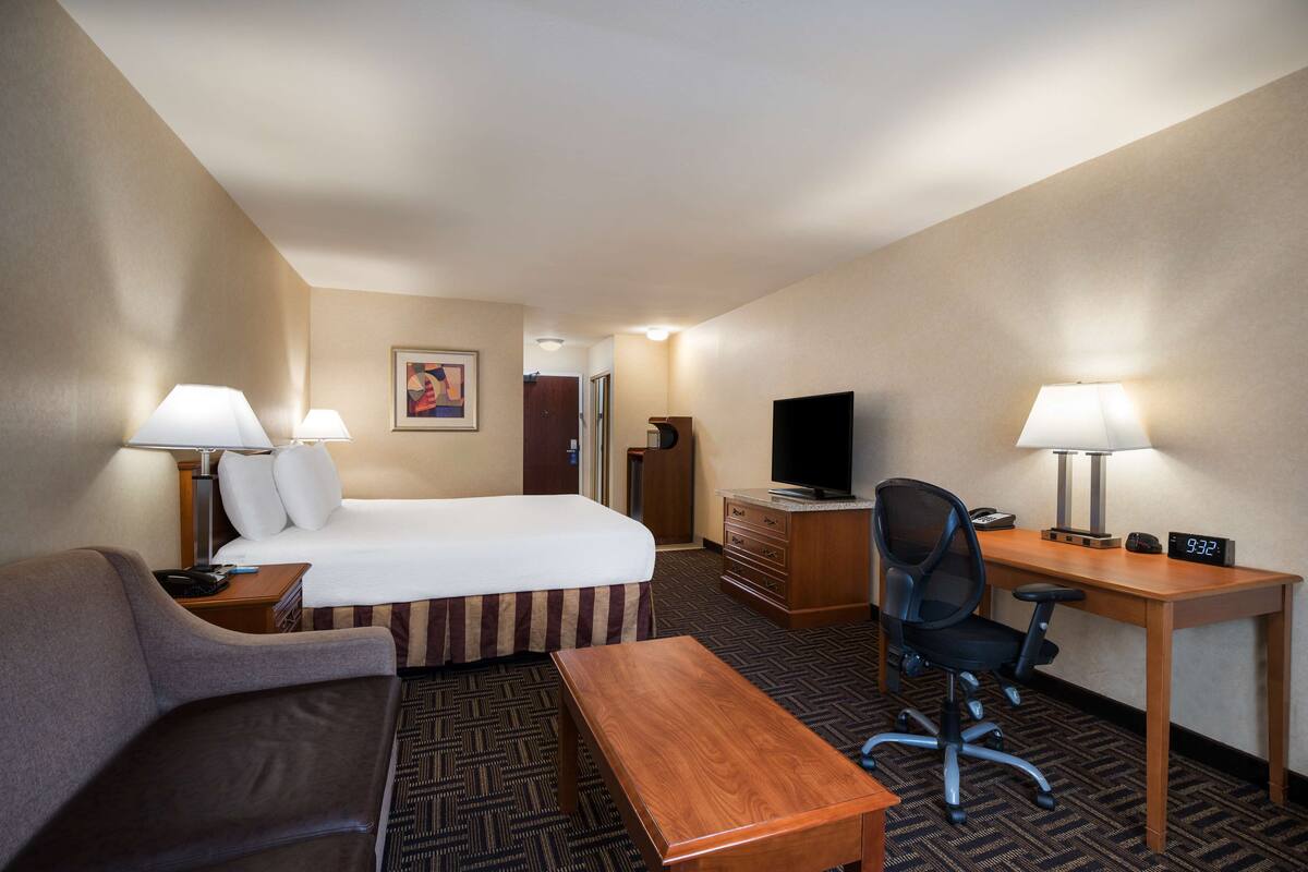 A hotel room with a bed, a desk with a computer, a chair, a TV, and two lamps.