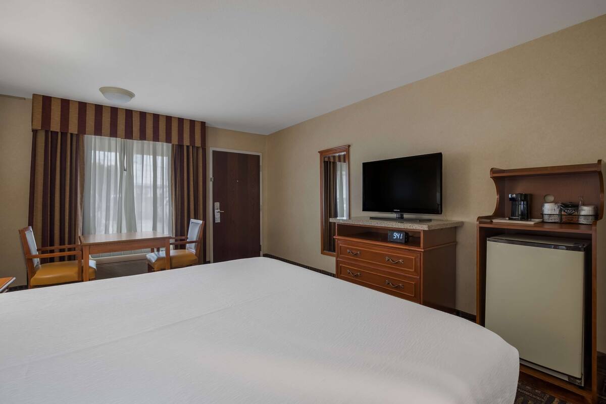 A hotel room with a large bed, a television, a desk with a chair, a small refrigerator, and a minibar.