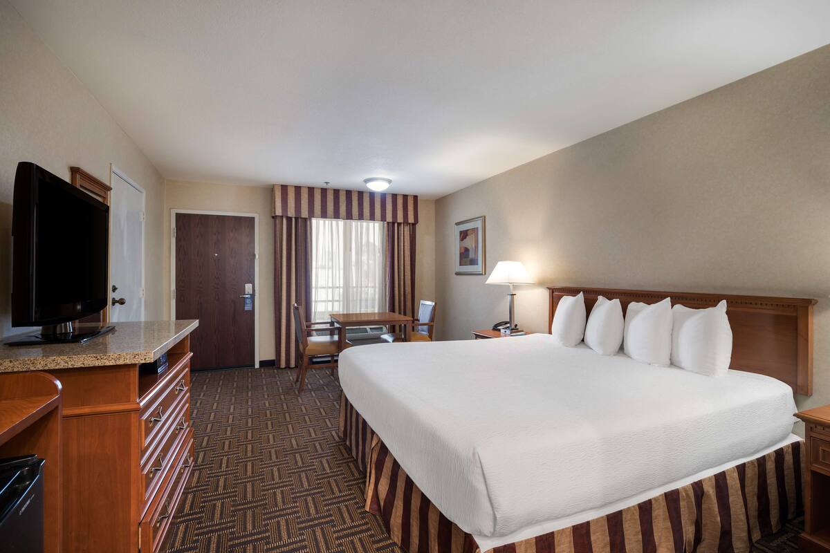 A hotel room with a large bed, a desk with a television, a chair, a desk lamp, and a door with curtains.