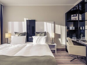 A hotel room with a large bed, two bedside tables, a chair, a bookshelf, and a window with curtains.