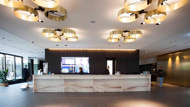 A modern reception desk with a marble top, surrounded by a spacious lobby with a high ceiling and circular lighting fixtures. - Mercure Hotel Wiesbaden City (Wiesbaden)
