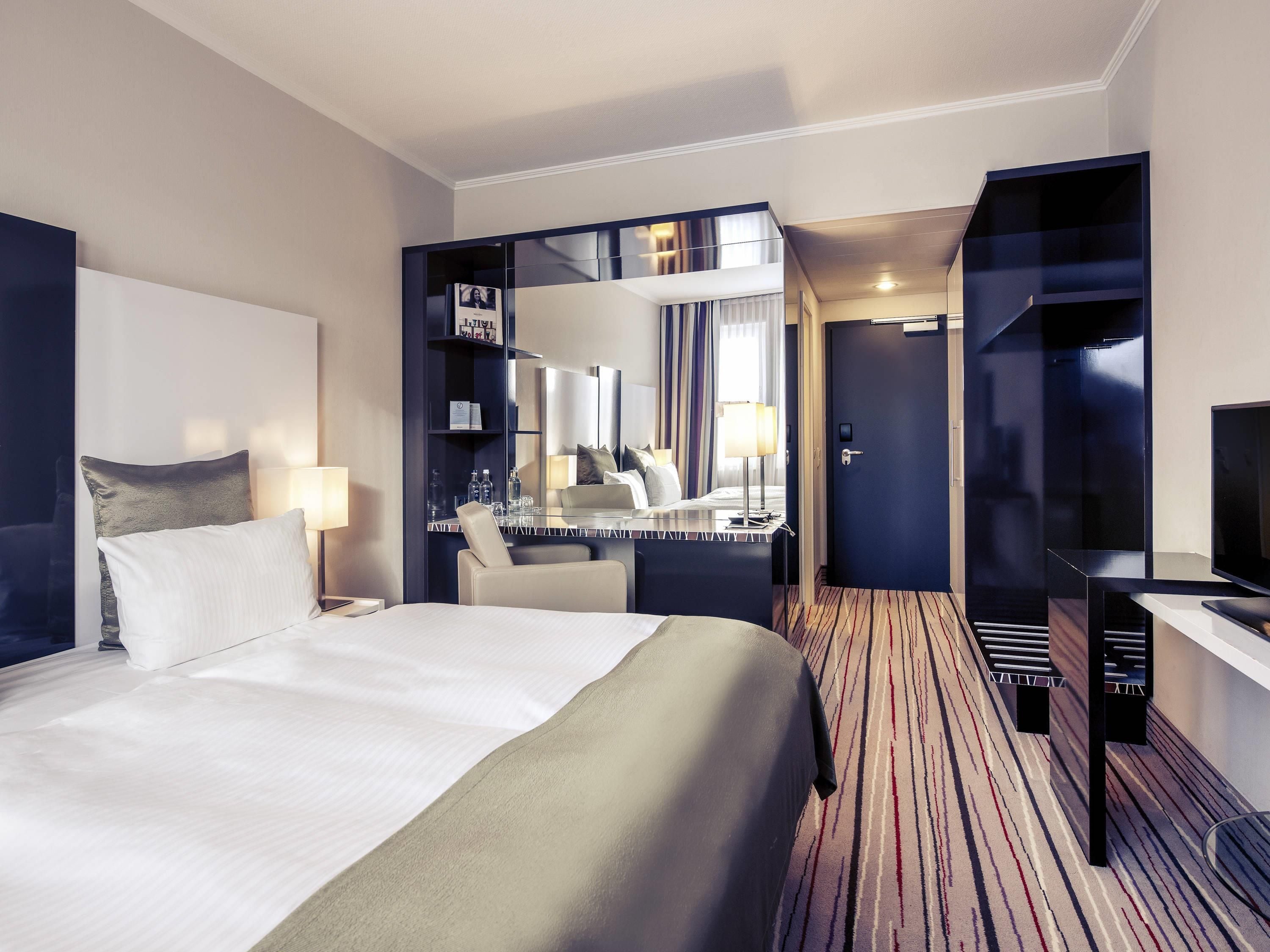 Ein Hotelzimmer mit einem großen Bett, einem Schreibtisch mit Stuhl, einem Spiegel und einem Kleiderschrank.
