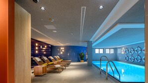 Un área de piscina interior moderna con tumbonas, un bar junto a la piscina y salvavidas en la pared.