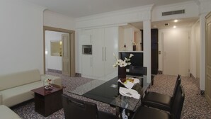 A hotel room with a dining table, a sofa, a TV, and a minibar. - Mercure Hotel Wiesbaden City (Wiesbaden)