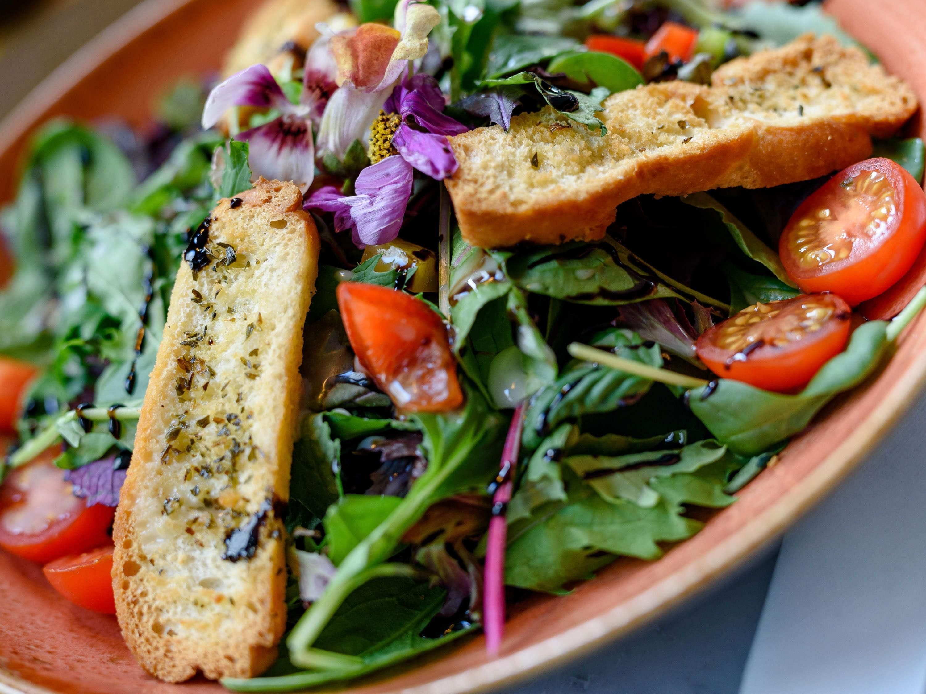 Un tazón de ensalada con diversas verduras, tomates cherry y trozos de pan.