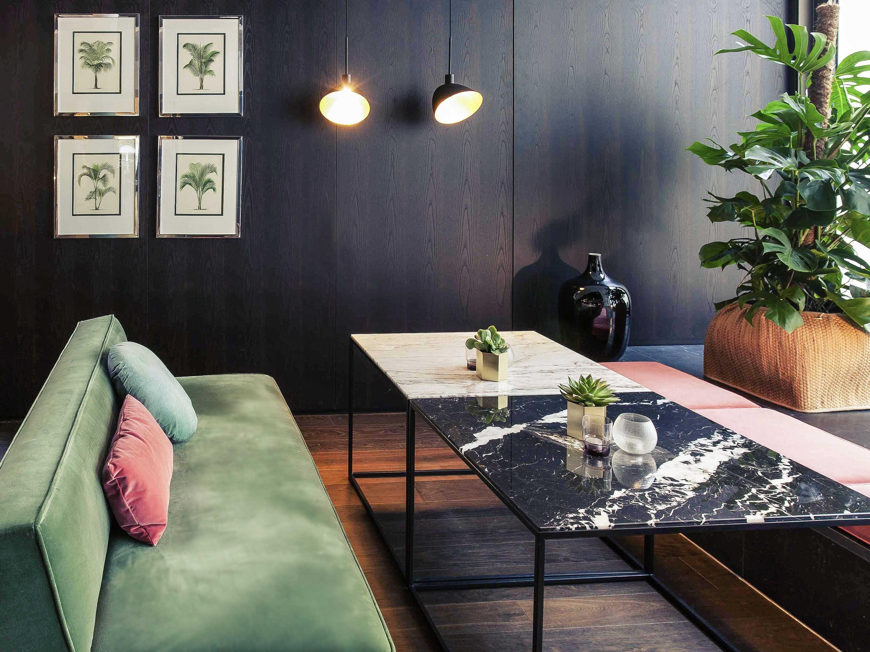 A modern interior with a green sofa, a marble table, and framed botanical prints on the wall.