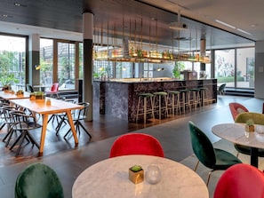A modern bar area with a marble countertop, bar stools, and a view of greenery outside. - Mercure Hotel Wiesbaden City (Wiesbaden)