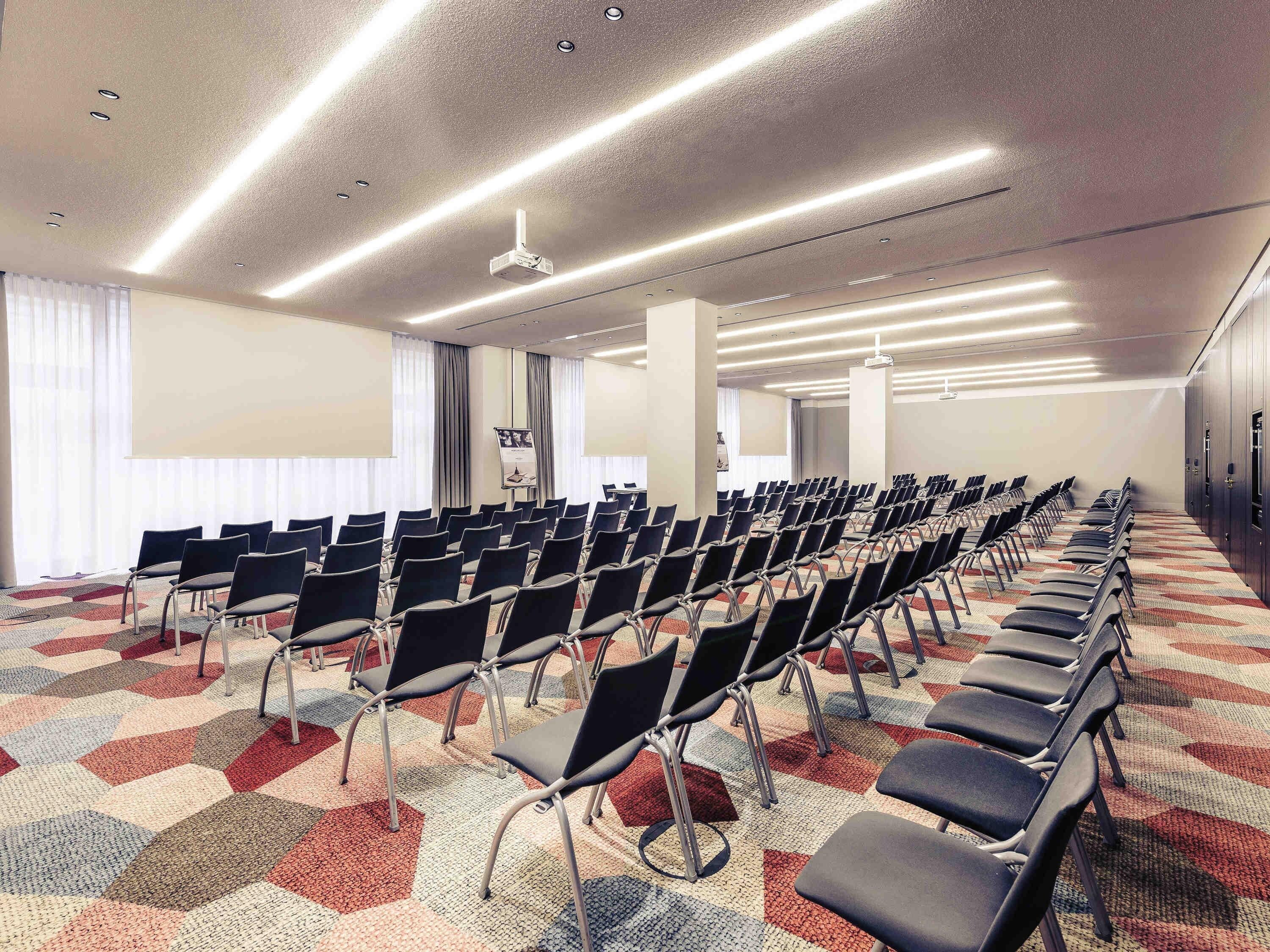 A conference room with rows of chairs, a projector screen, and a carpeted floor.