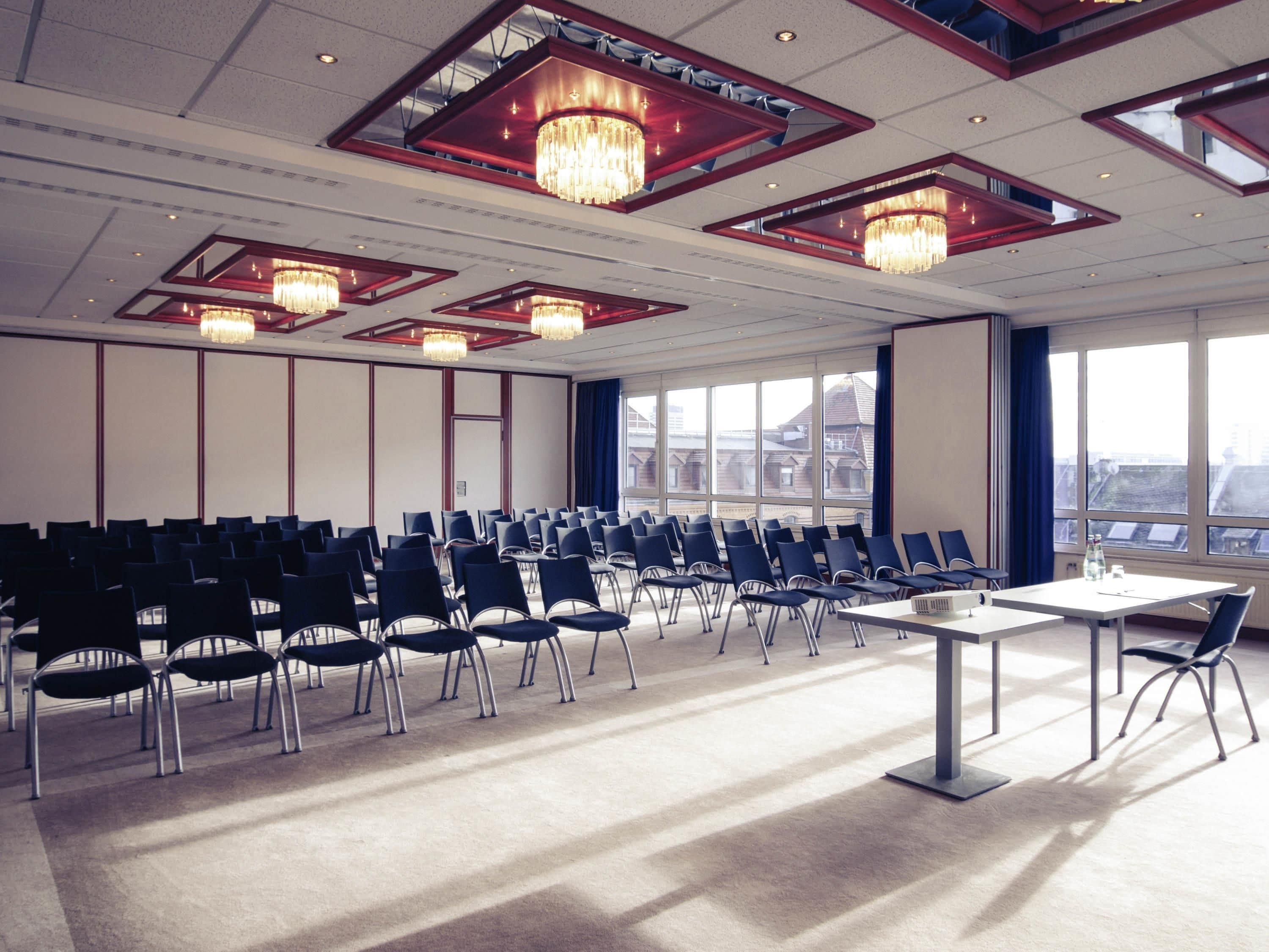 Un salón de conferencias con filas de sillas, una mesa y candelabros.