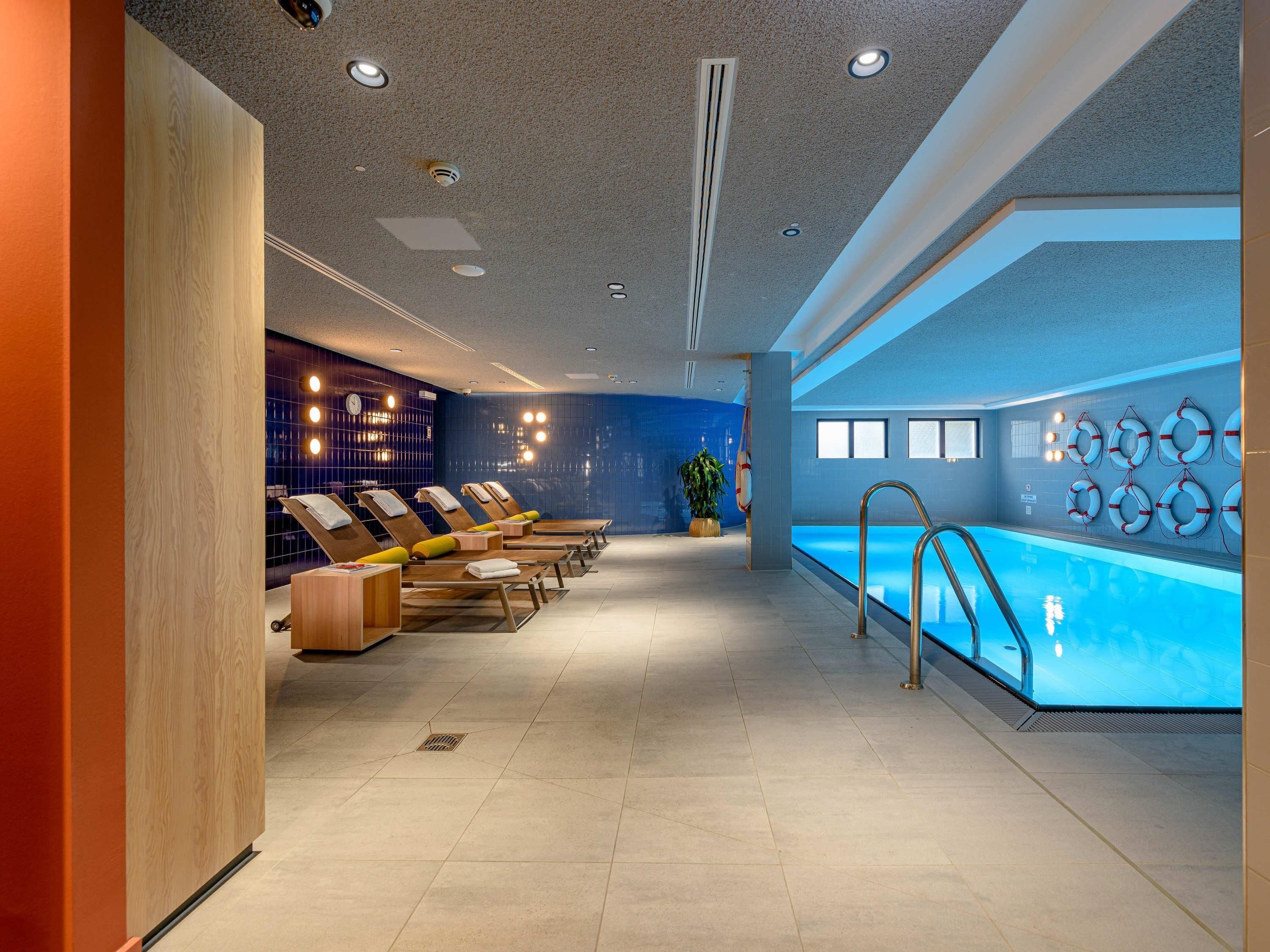 Ein moderner Poolbereich im Innenbereich mit Liegestühlen, einer Poolbar und Rettungsringen an der Wand.