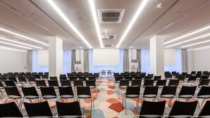 A conference room with rows of black chairs, a colorful carpet, and a projector screen at the front. - Mercure Hotel Wiesbaden City (Wiesbaden)