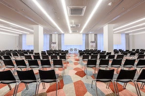 A conference room with rows of black chairs, a colorful carpet, and a projector screen at the front. - Mercure Hotel Wiesbaden City (Wiesbaden)
