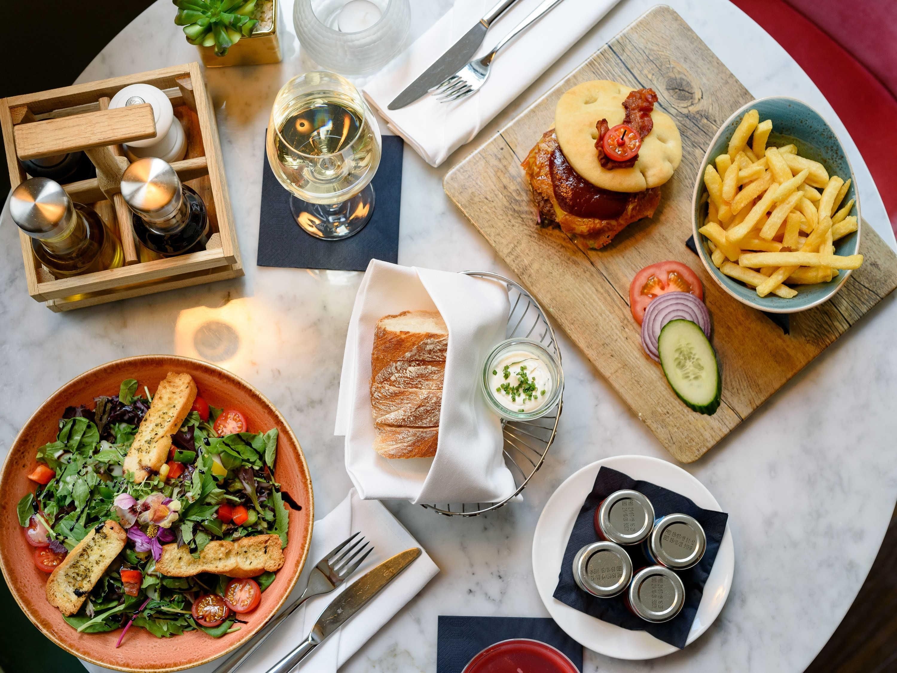 Ein Tisch reichhaltig gedeckt mit verschiedenen Speisen, darunter Salat, Brot, ein Sandwich, Pommes und Soßen.