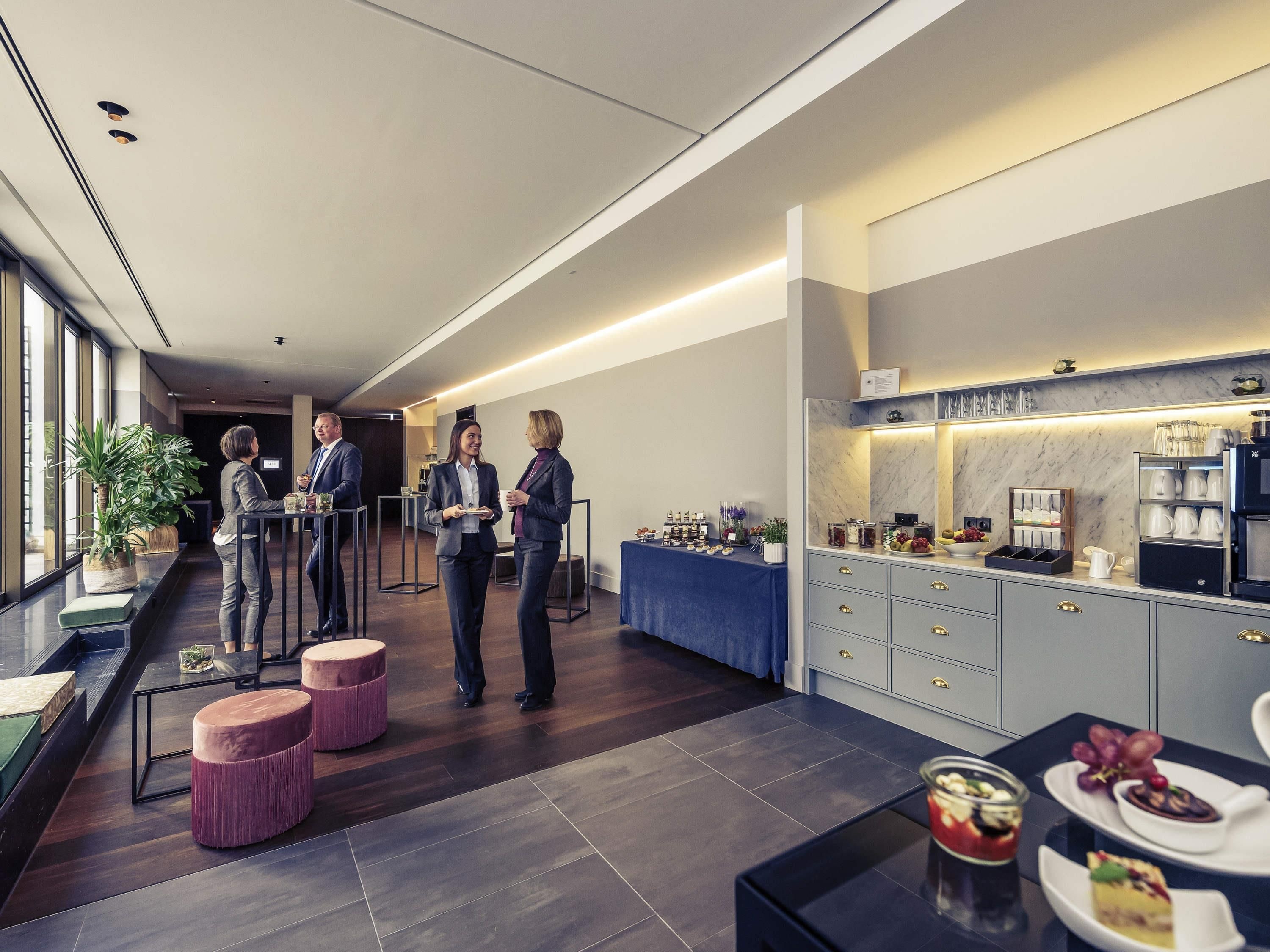 A modern hotel lobby with a reception desk, seating area, and a buffet with various food items.