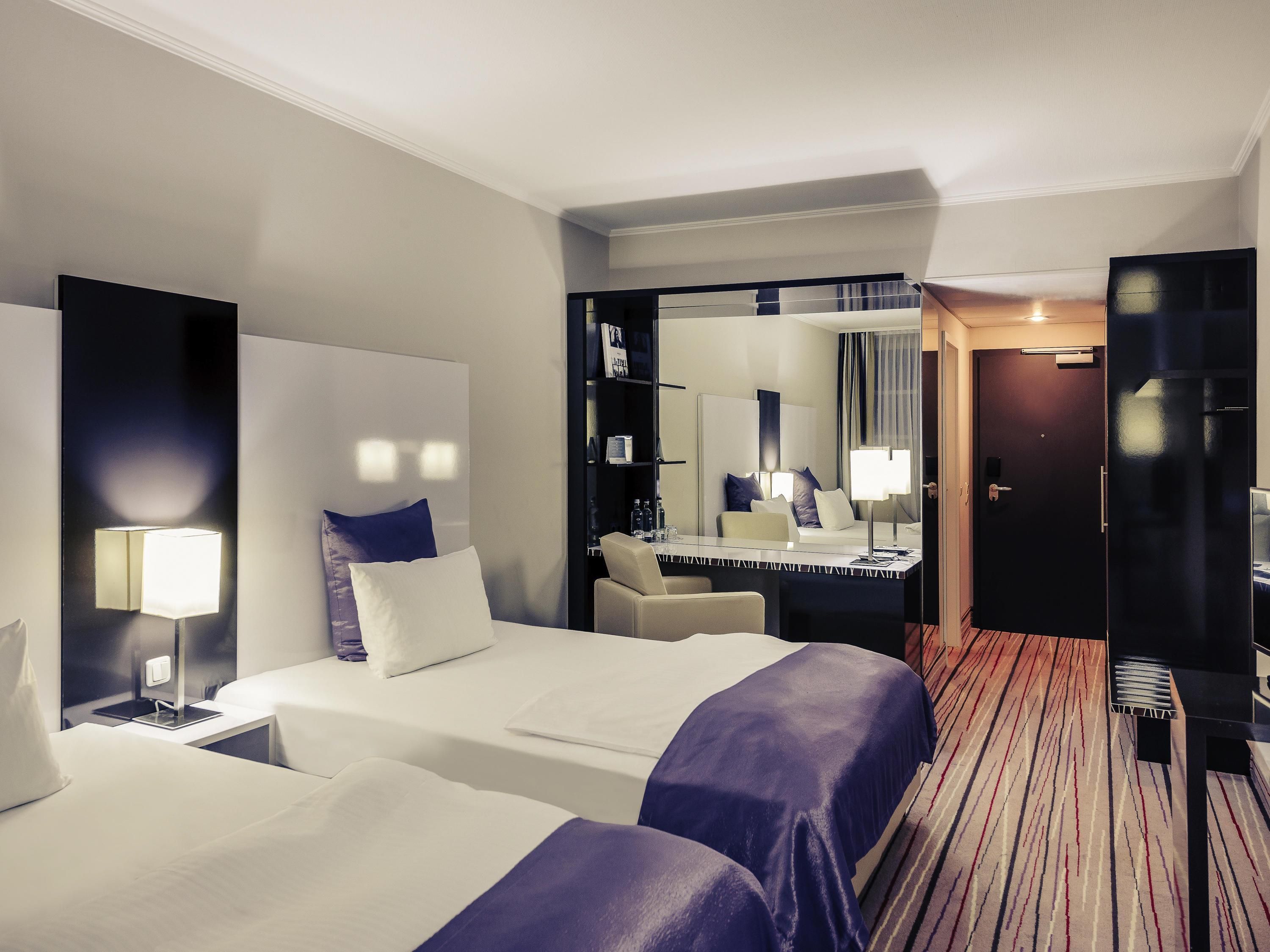 Une chambre d’hôtel avec deux lits, un bureau, une chaise, un miroir et une porte.