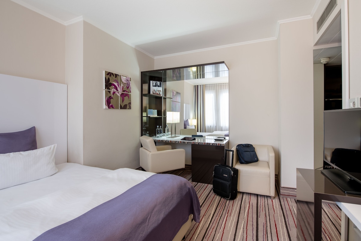A hotel room with a bed, a desk, a chair, a suitcase, and a television.