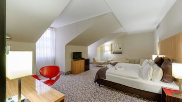A hotel room with a bed, a desk, a red chair, a television, and a small table.