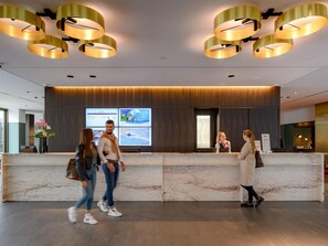 A hotel reception area with marble counters, modern pendant lighting, and digital displays. - Mercure Hotel Wiesbaden City (Wiesbaden)