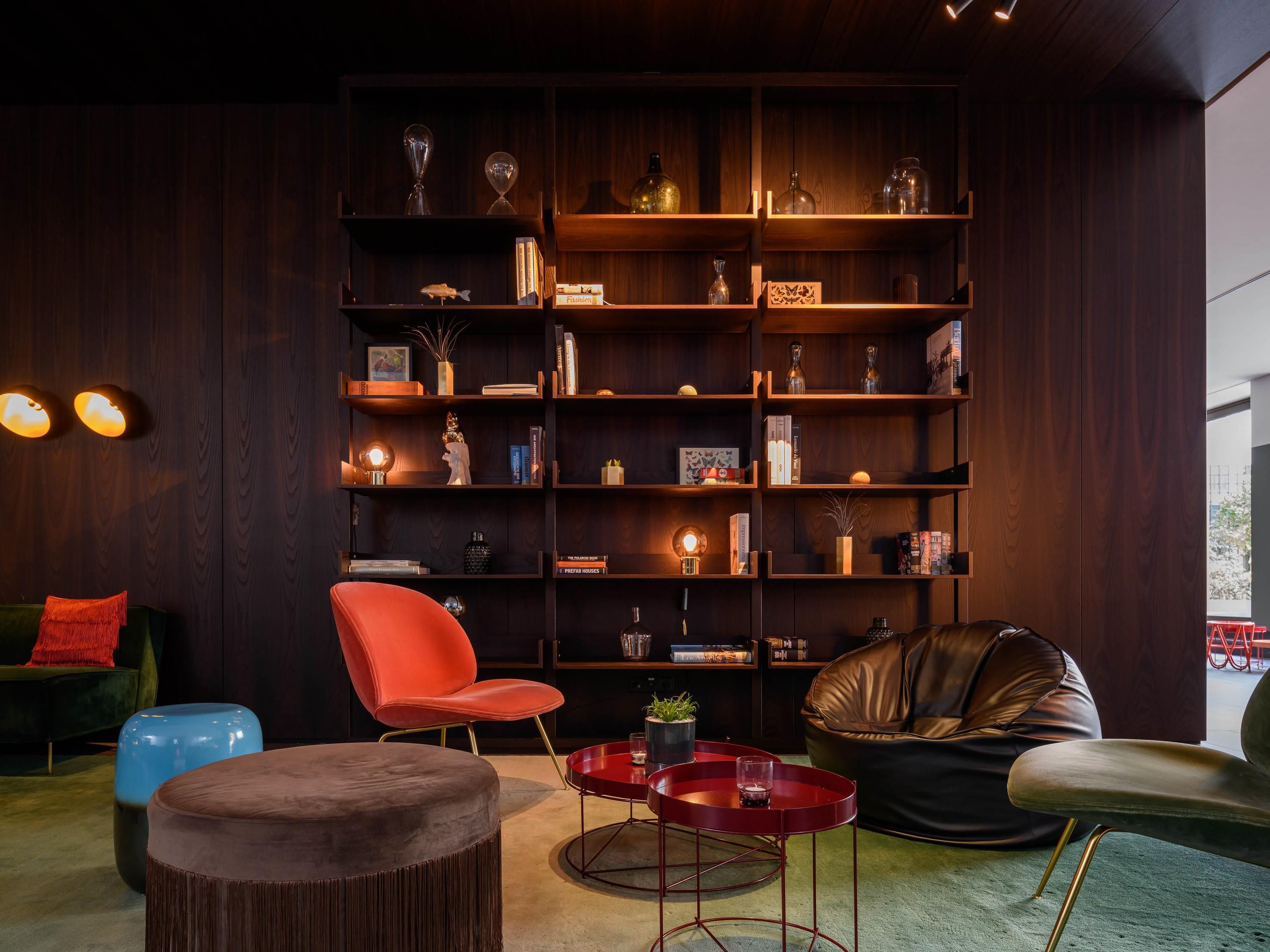 A modern living room with a dark wood bookshelf, red and black chairs, and a round coffee table.