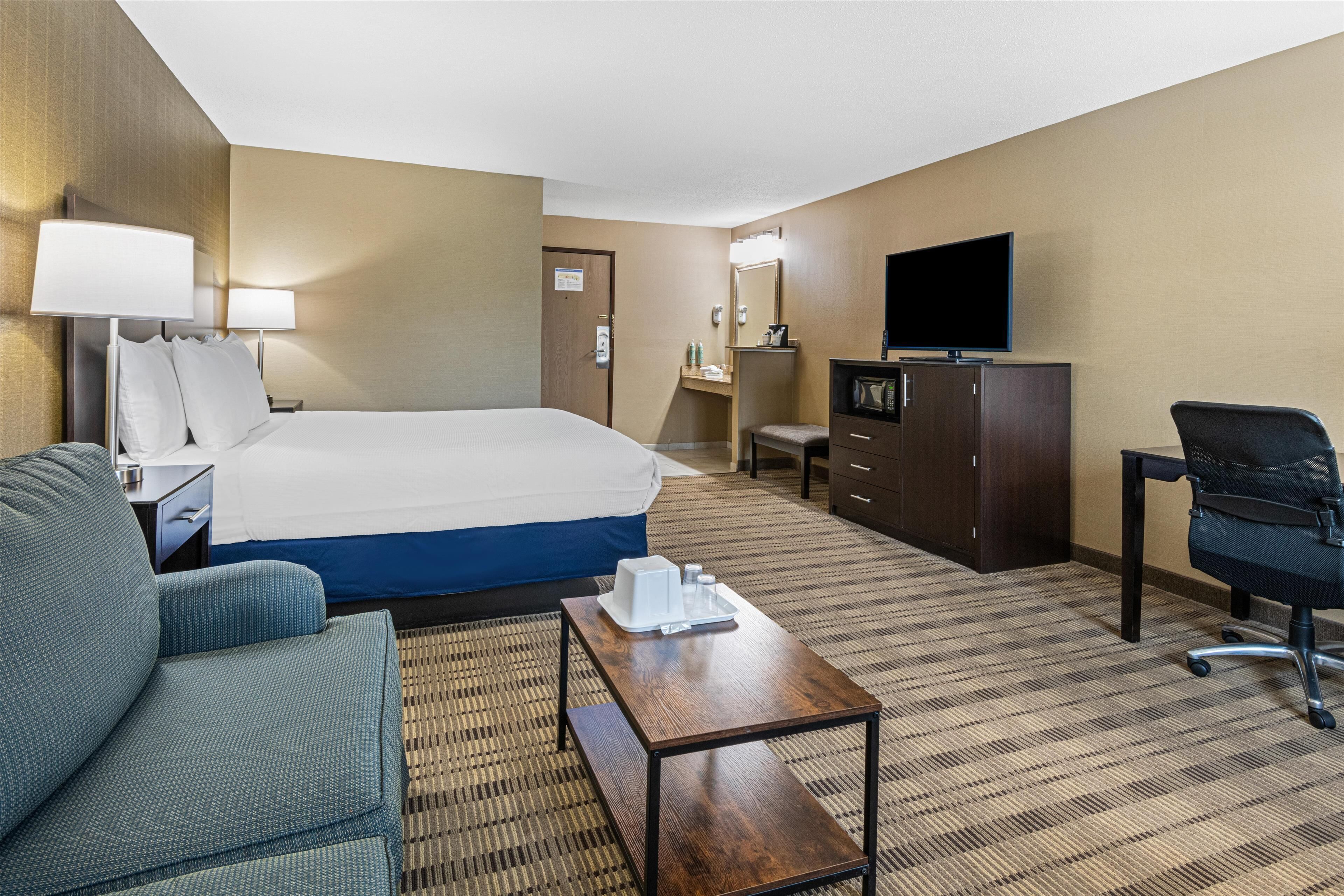 A hotel room with a bed, a desk, a chair, a television, and a minibar.