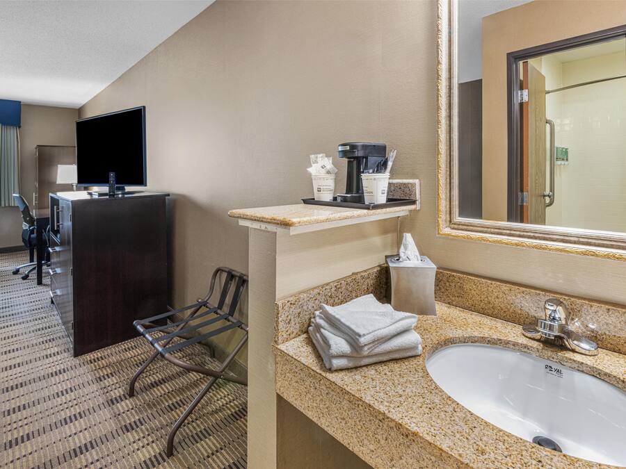 A hotel room with a desk, television, and a bathroom with a sink and mirror.