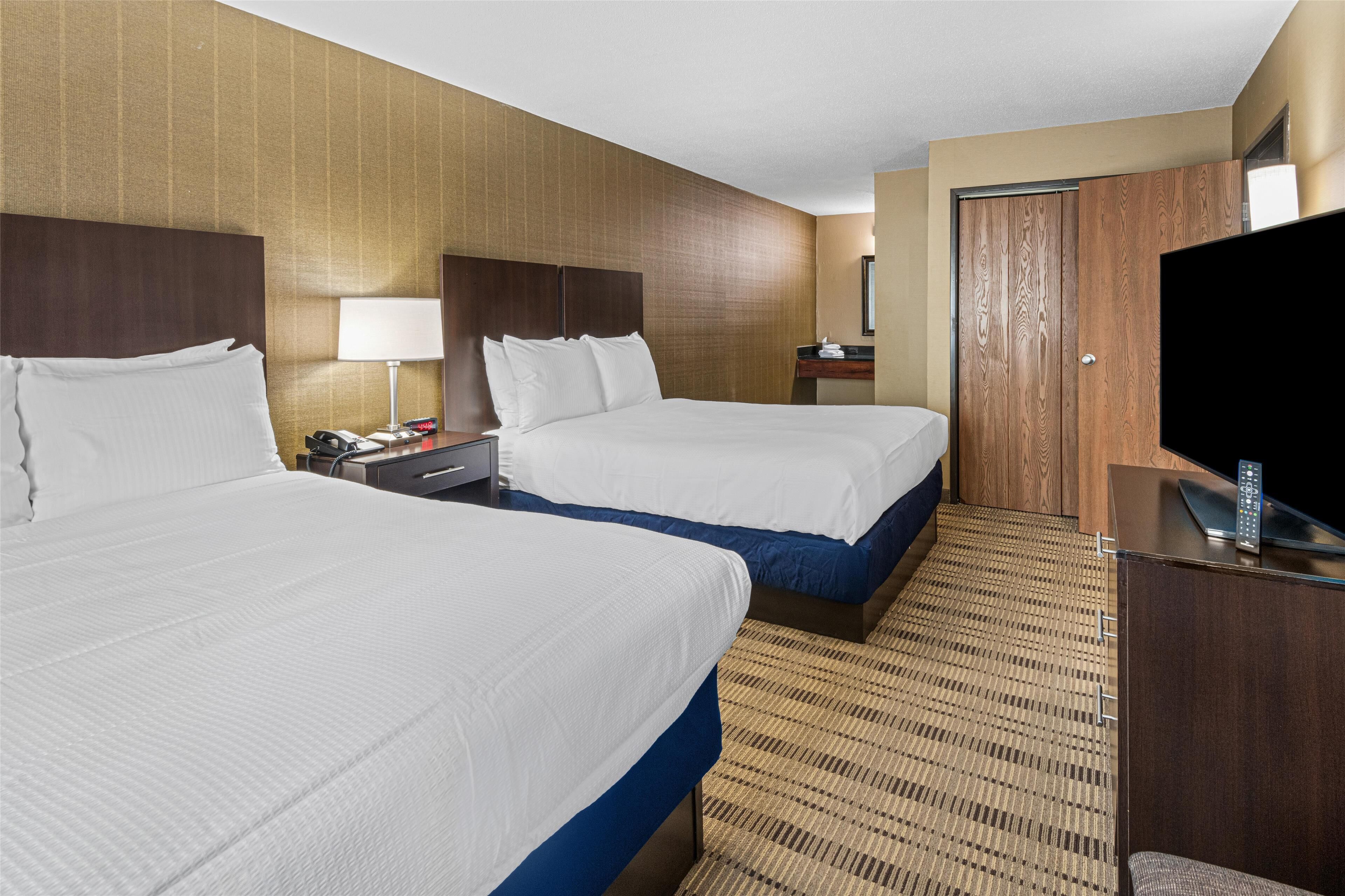 A hotel room with two beds, a desk with a lamp, a TV, and a wardrobe.