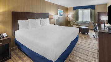 A hotel room with a large bed, a desk, a chair, a TV, and a window with curtains.