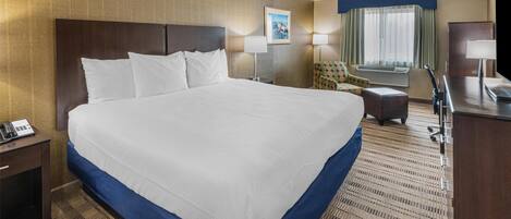 A hotel room with a large bed, a desk, a chair, a TV, and a window with curtains.