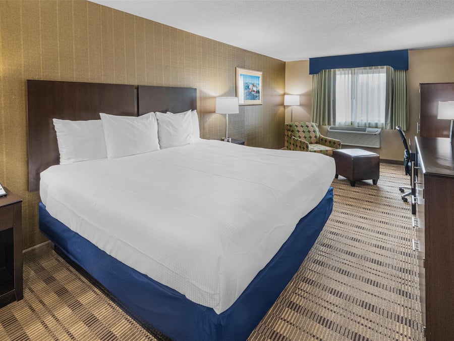 A hotel room with a large bed, a desk, a chair, a TV, and a window with curtains.