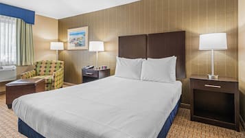 A hotel room with a large bed, two bedside tables, a chair, and a lamp.