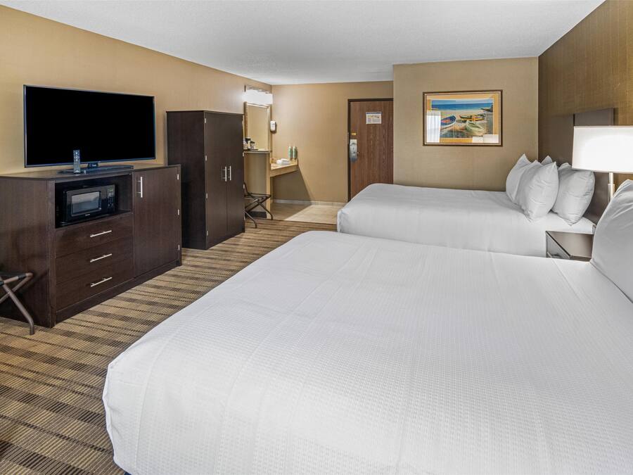 A hotel room with two beds, a TV, a microwave, a desk, and a painting on the wall.