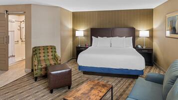 A hotel room with a large bed, two nightstands, a wooden coffee table, a patterned armchair, a blue sofa, and a shower area.