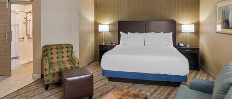 A hotel room with a large bed, two nightstands, a wooden coffee table, a patterned armchair, a blue sofa, and a shower area.