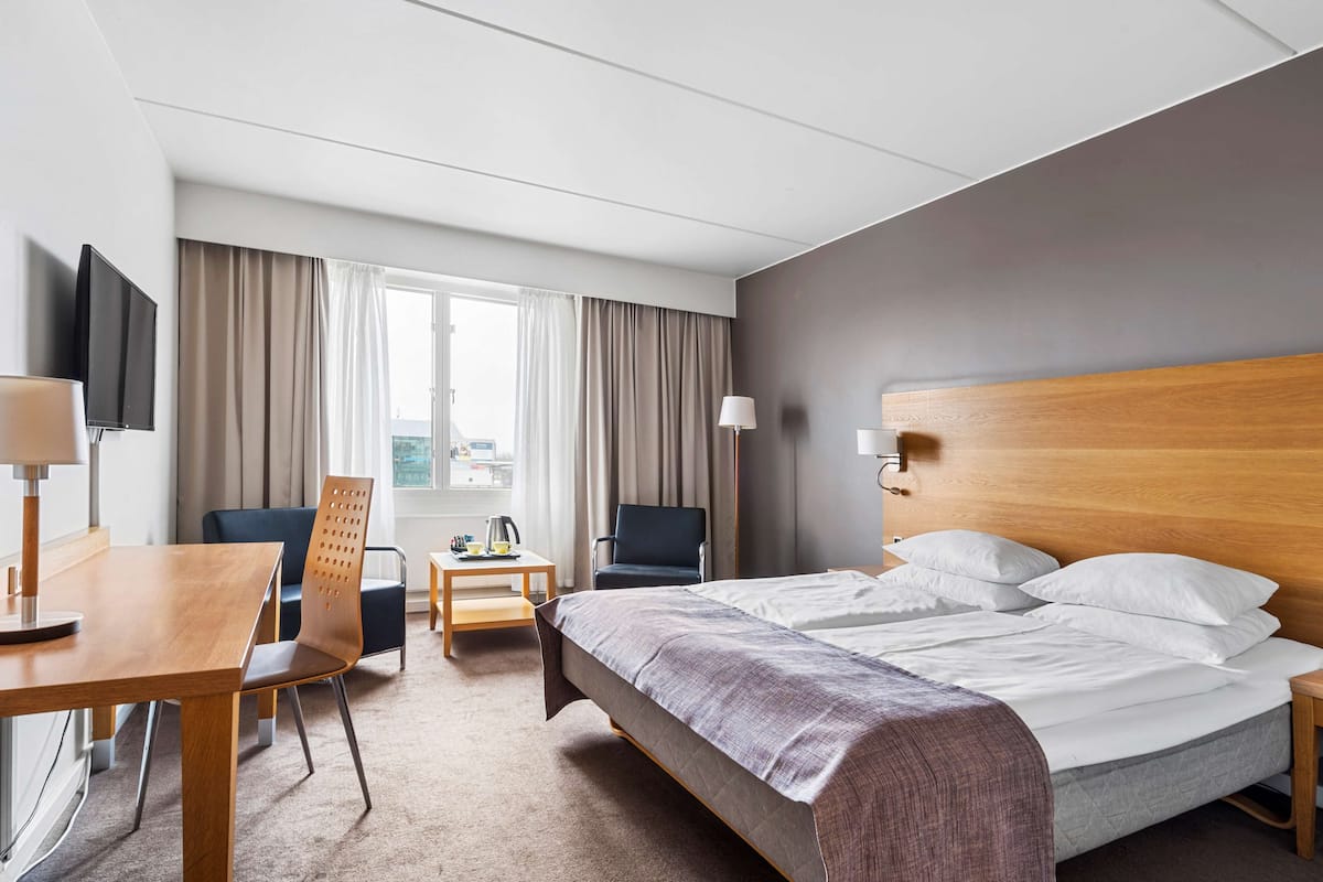 Une chambre d’hôtel avec un lit, un bureau, une chaise, une télévision et une fenêtre avec des rideaux.