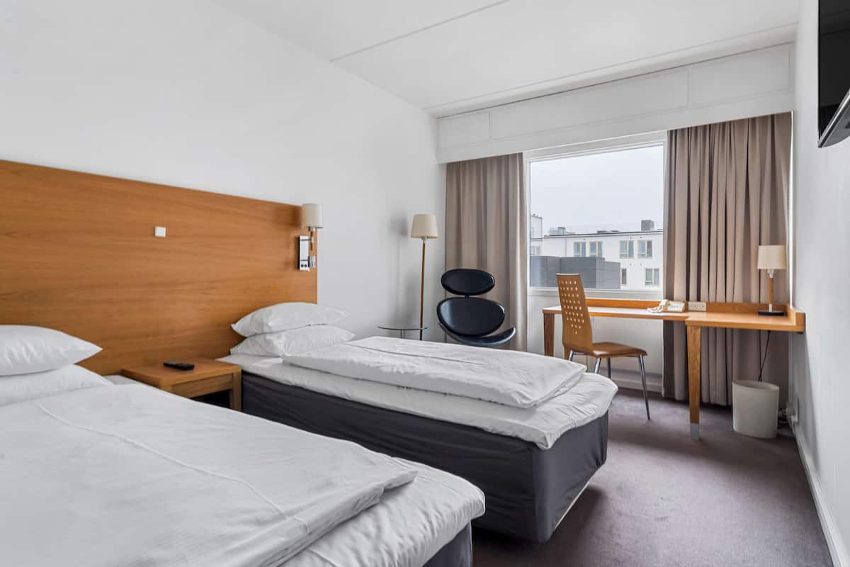 Une chambre d’hôtel avec deux lits, un bureau, une chaise et une fenêtre avec des rideaux.