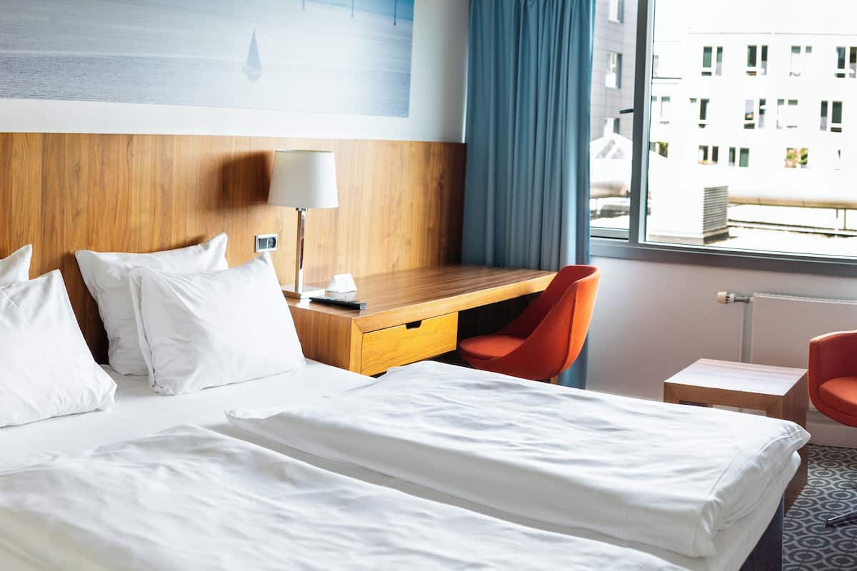 Une chambre d’hôtel avec un lit, un bureau, deux chaises et une fenêtre donnant sur des immeubles.