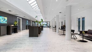 Een ruime lobby met een hoge plafond, een modern receptiebalie, een zithoek en grote ramen die natuurlijk licht binnenlaten.