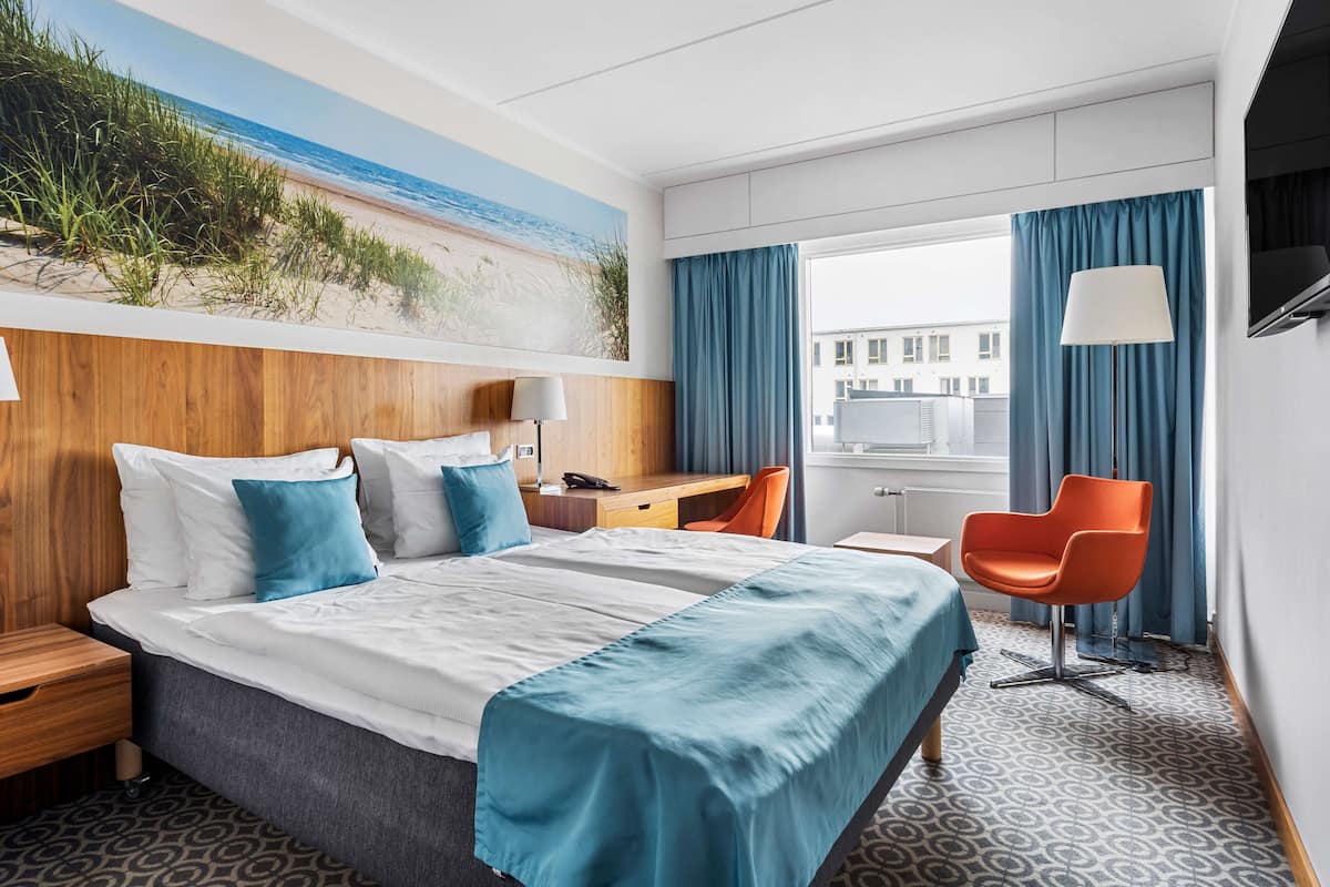Une chambre d’hôtel avec un grand lit, un bureau, une chaise et une fenêtre avec des rideaux.