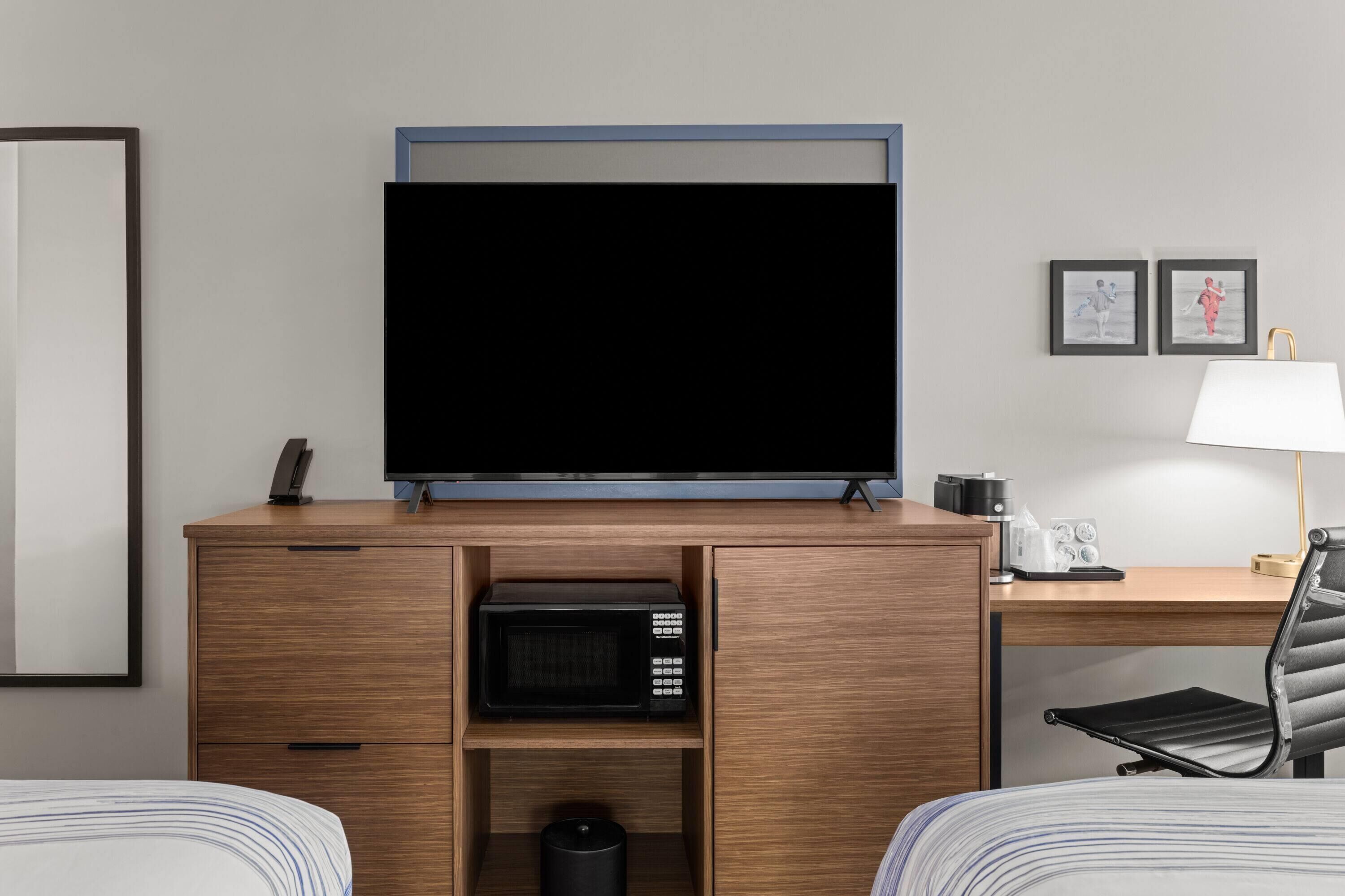 Ein Hotelzimmer mit Flachbildfernseher, Mikrowelle, Schreibtisch mit Lampe und zwei Betten.
