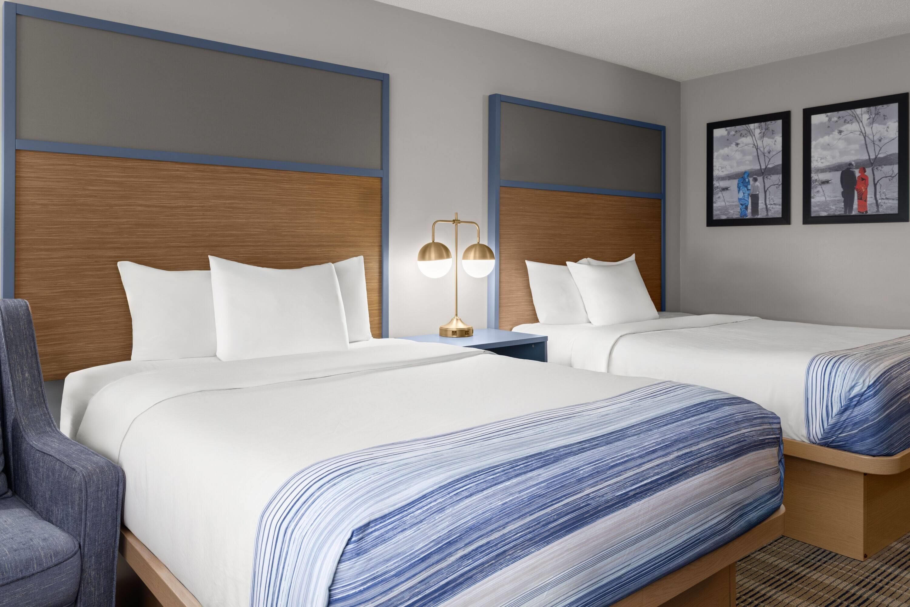 Ein Hotelzimmer mit zwei Betten, einem Nachttisch, einer Lampe und einem Sessel.