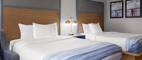 A hotel room with two beds, a nightstand, a lamp, and a chair.