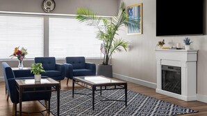 A living room with a fireplace, two blue armchairs, a coffee table, a patterned rug, and a large TV on the wall.