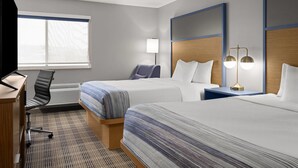 A hotel room with two beds, a desk, a chair, a lamp, and a window.