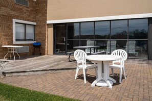A patio with a table and chairs, a barbecue grill, and a building with large windows. - AmericInn by Wyndham Marshfield (Marshfield)