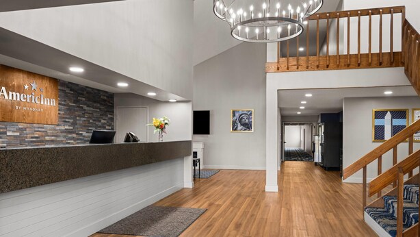 A reception area with a wooden reception desk, a chandelier, a staircase, and a hallway leading to other rooms.