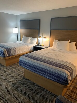A hotel room with two beds, a nightstand with a lamp, and a patterned carpet.