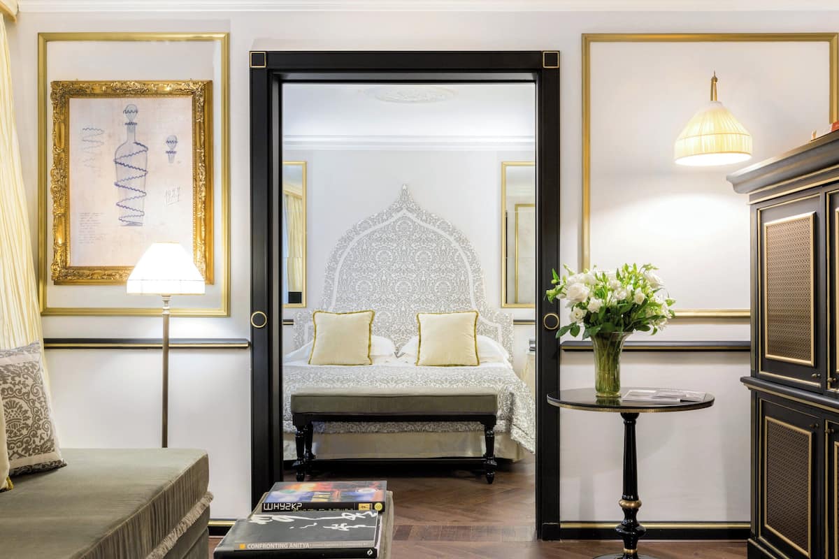 A hotel room with a bed, bedside table, lamp, and a vase with flowers.