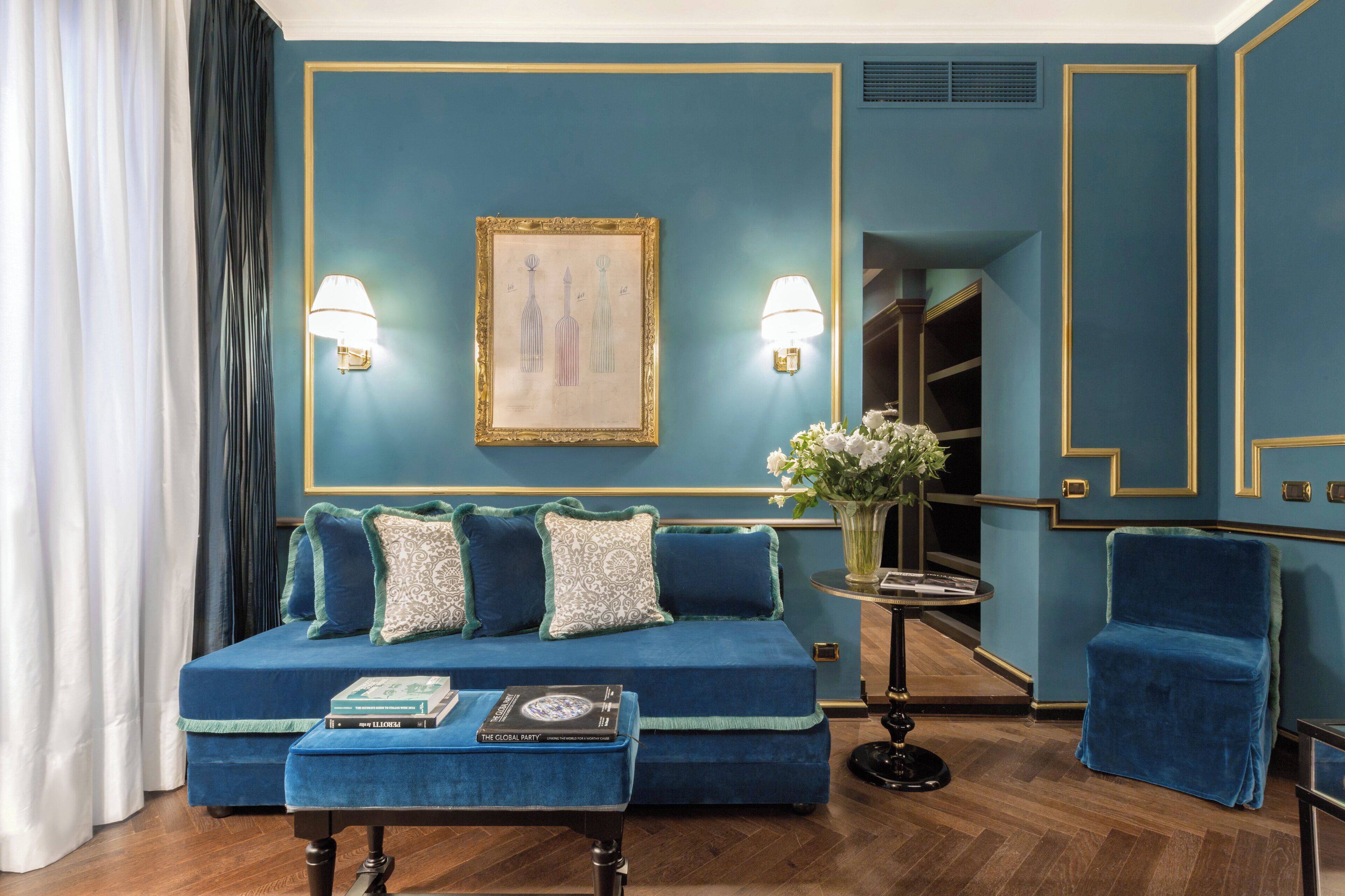 Una habitación con un sofá azul, un sillón a juego, una pequeña mesa redonda con un florero y un cuadro en la pared.