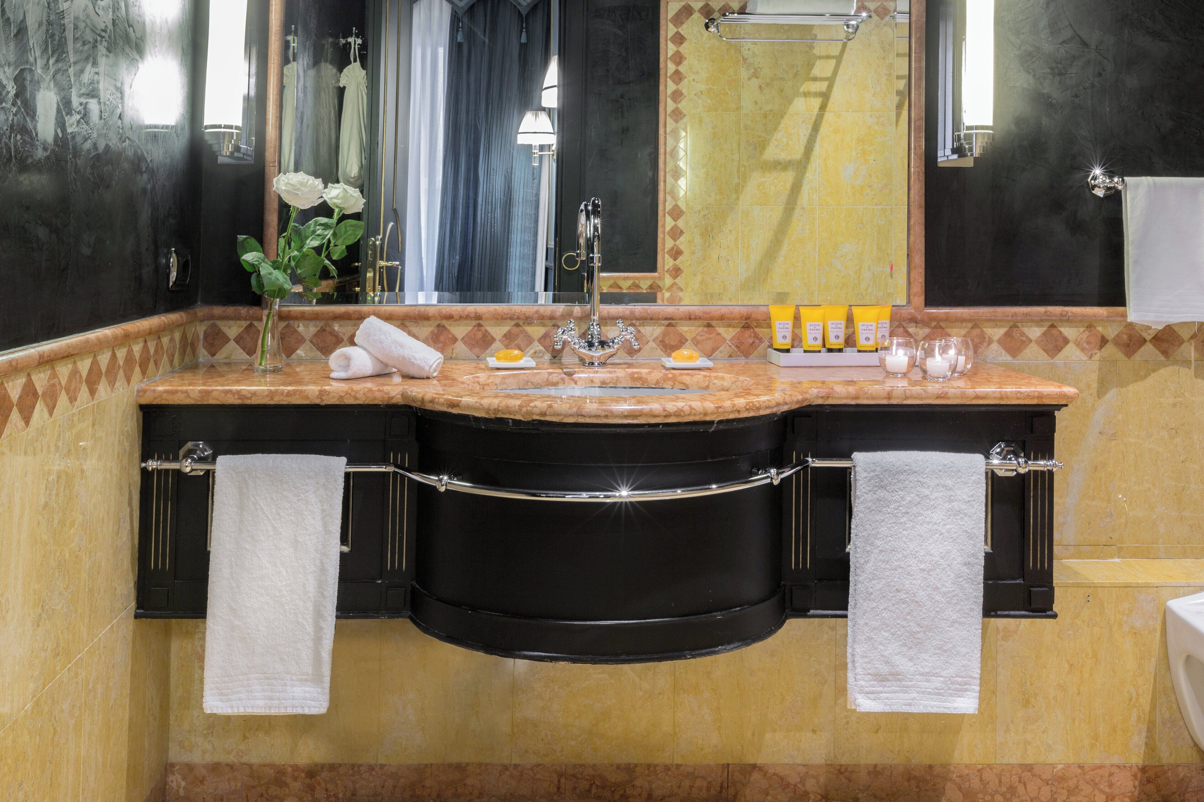A bathroom with a black vanity, two sinks, a mirror, a towel rack, and toiletries.