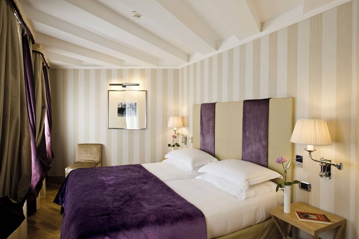 A hotel room with a large bed, a chair, a bedside table with a lamp, and a mirror on the wall.